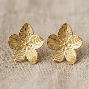 Peut inclure: Une paire de boucles d'oreilles à clous en forme de fleur dorée. Chaque boucle d'oreille présente un design à cinq pétales avec des nervures détaillées et un centre texturé. Les boucles d'oreilles sont en métal brillant.