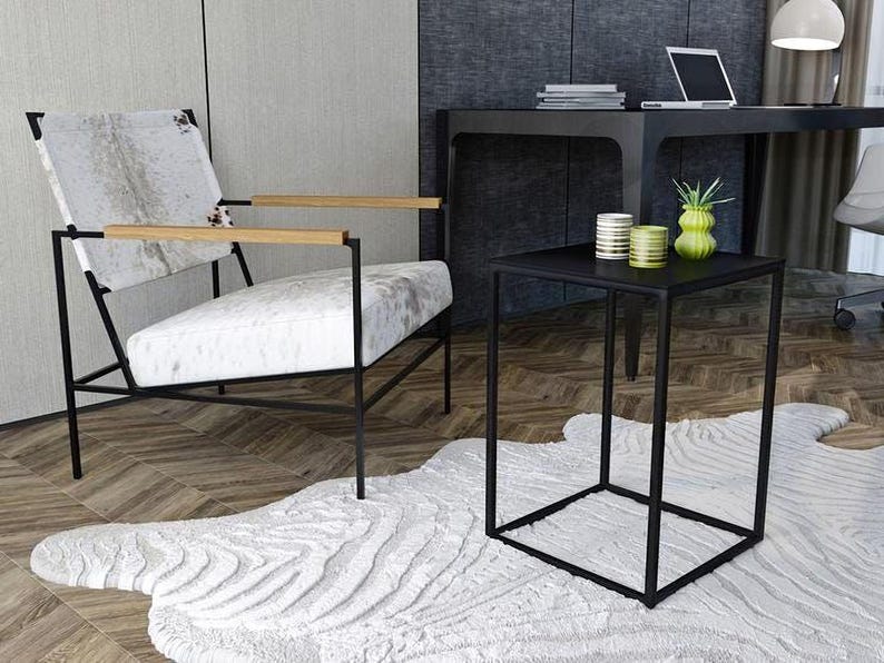 a modern living room with a white cowhide rug, a black metal side table, and a white leather chair with wooden armrests.