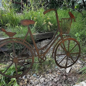 A rusted metal bicycle sculpture stands in a grassy area, with a bird perched on the handlebars.