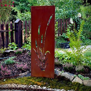 A red metal sculpture with a plant design stands in a lush garden surrounded by various plants and flowers.