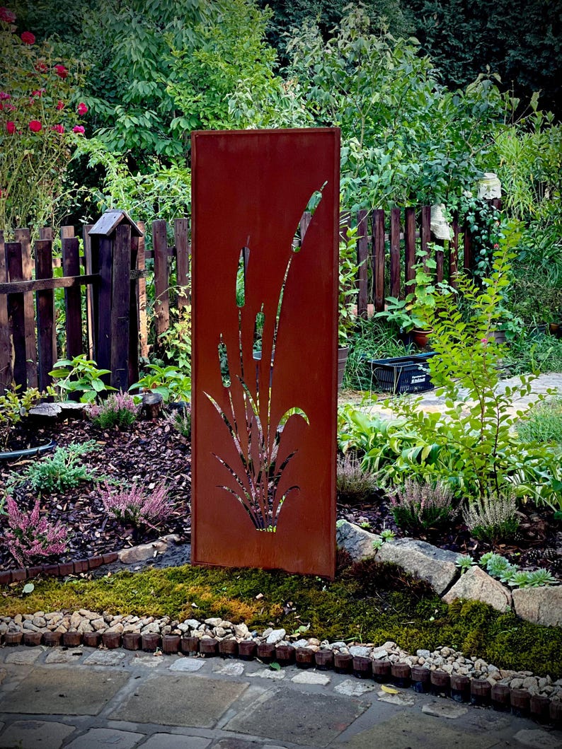 A red metal sculpture with a plant design stands in a lush garden surrounded by various plants and flowers.