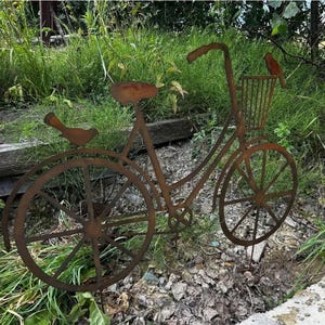A rusted metal bicycle sculpture stands in a grassy area, with a bird perched on the handlebars.