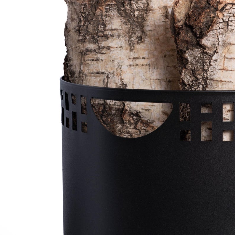 May include: A black metal log holder with a decorative cut-out design. The holder encases birch logs, showcasing the natural bark texture. The design features a curved top and a cylindrical shape, providing a modern aesthetic.
