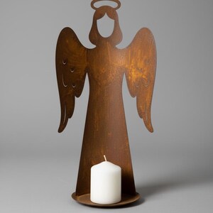 Peut inclure: Un bougeoir ange en métal rouillé avec une bougie pilier blanche. La silhouette de l'ange a des ailes et une auréole, et le métal a une finition marron vieillie. La bougie repose sur une base circulaire.