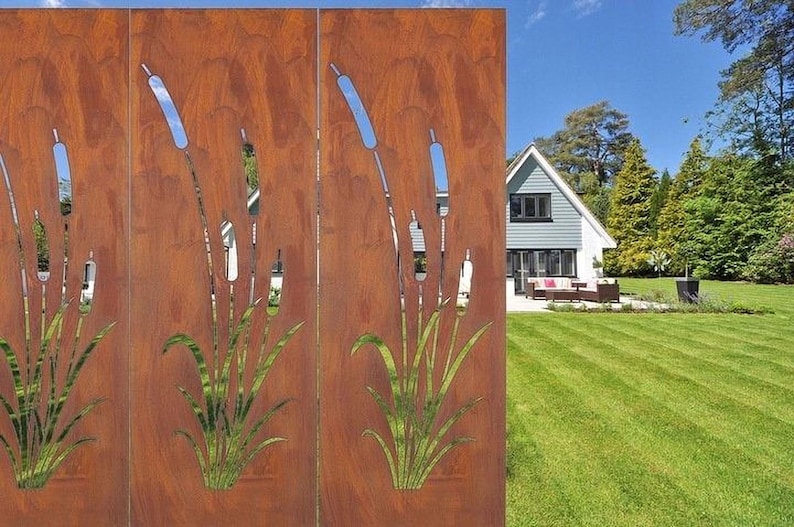 a rust-colored metal fence with a design of reeds or grasses on it, set against a backdrop of a well-maintained lawn and a house surrounded by trees.