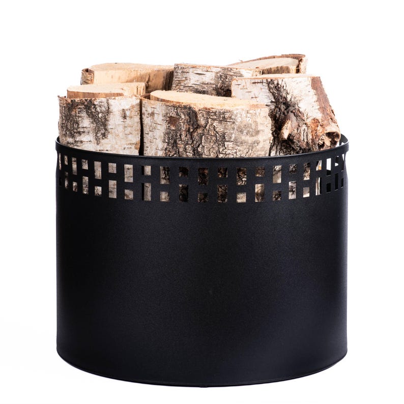 May include: A black metal log holder filled with birch firewood. The cylindrical holder has a decorative square cut-out pattern near the top. The birch logs are light brown and white, with visible bark.