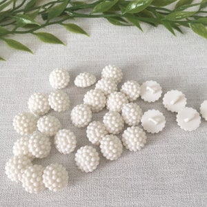 May include: A collection of 20 white plastic buttons with a textured, raised dot design. The buttons are arranged in a semi-circle on a white surface.