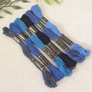 May include: Six spools of embroidery floss in shades of blue, from dark navy to light blue. The spools are labelled with the brand name "EKO IMPORT" and the thread number.