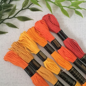 May include: Six spools of embroidery floss in shades of orange, yellow, and red. The spools are labelled with the brand names "Duchess" and "Trebla".