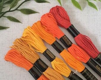 Puede incluir: Seis carretes de hilo de bordar en tonos naranja, amarillo y rojo. Los carretes están etiquetados con las marcas "Duchess" y "Trebla".