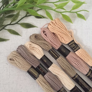 May include: Six spools of embroidery floss in various shades of beige, brown, and pink. The spools are labelled with the brand name "DMC" and the colour numbers.