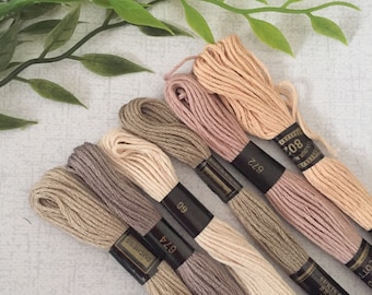 Puede incluir: Seis carretes de hilo de bordar en varios tonos de beige, marrón y rosa. Los carretes están etiquetados con el nombre de la marca "DMC" y los números de color.