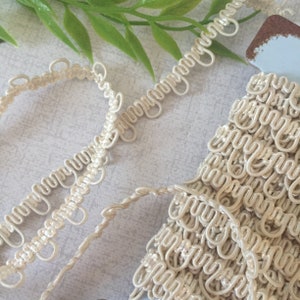 May include: Close-up of ivory white decorative trim with a looped design. The trim is made of a soft, flexible material and is perfect for adding a touch of elegance to any project.