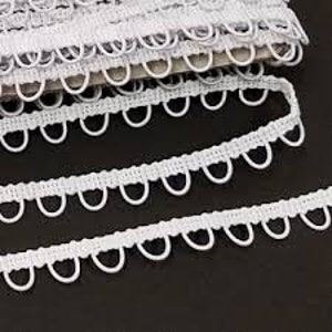May include: White elastic trim with a scalloped edge and small loops. The trim is folded and stacked on a white surface.