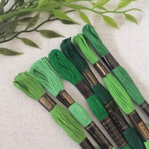 May include: Six spools of green embroidery floss, arranged in a gradient from light to dark green. The spools are labeled with the brand name "TREBLA" and the color number.