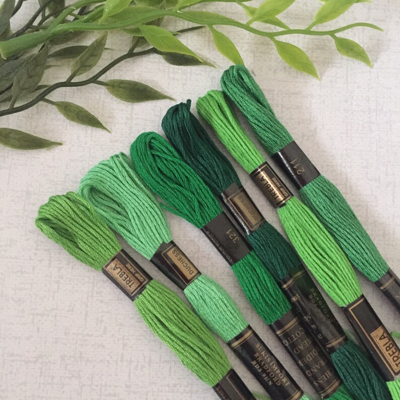 May include: Six spools of green embroidery floss, arranged in a gradient from light to dark green. The spools are labeled with the brand name "TREBLA" and the color number.