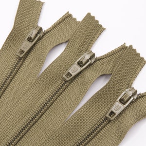 May include: Three olive green zipper closures with metal sliders. The zippers are laid out in a row, with the sliders facing the viewer.
