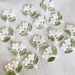 May include: A collection of white embroidered flower appliques with green leaves. The flowers have a delicate lace-like design and are perfect for adding a touch of elegance to any project.
