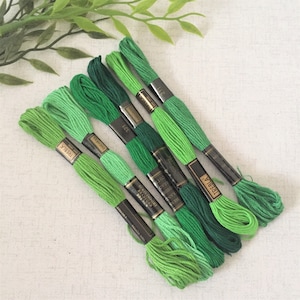 May include: Six spools of green embroidery floss, arranged in a gradient from light to dark green. The spools are labeled with the brand name "TRESBIA" and the color number.