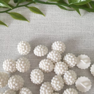 May include: A collection of white plastic buttons with a textured, bumpy surface. The buttons are round and have a diameter of approximately 1 inch.