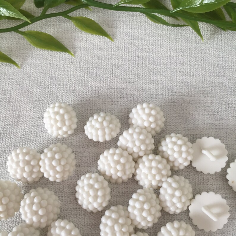 May include: A collection of white plastic buttons with a textured, bumpy surface. The buttons are round and have a diameter of approximately 1 inch.
