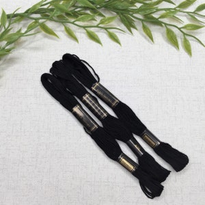 May include: Three spools of black embroidery floss with gold labels that read "Suki Import Embroidery Floss" and "Duchiness 420".