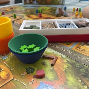 May include: A close-up of a board game with a red, white, and green tray, a green, blue, and orange bowl, and wooden pieces. The numbers 54-59 are visible on the board.