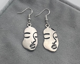 May include: A pair of silver earrings with a face outline design. The earrings are dangle style with a hook closure.