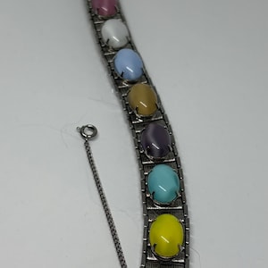 May include: A silver-toned bracelet featuring a series of colorful, oval-shaped stones. The stones are in shades of green, pink, white, blue, yellow, brown, purple, and turquoise. The bracelet has a clasp closure and a safety chain.