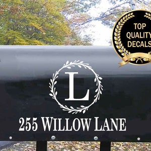 May include: Black mailbox with a white wreath and the letter L in the center. The mailbox also has the address 255 Willow Lane printed below the wreath.