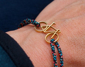 May include: A gold bicycle charm bracelet with a black, blue, and red braided cord.