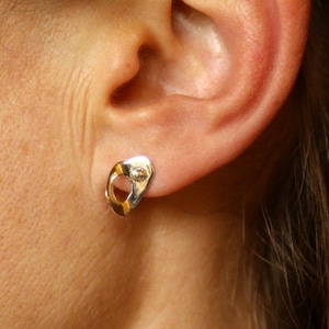 Peut inclure: Une paire de boucles d'oreilles en argent avec un design abstrait unique. Les boucles d'oreilles sont petites et délicates, et elles ont une surface légèrement texturée.