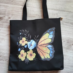 以下が含まれることがあります： カラフルな蝶と花の刺繍が施された黒いキャンバス地のトートバッグです。