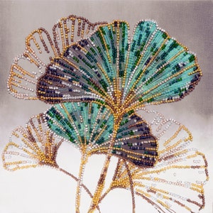 Könnte beinhalten: Nahaufnahme eines Perlenbildes mit drei Ginkgoblättern. Die Blätter bestehen aus kleinen, bunten Perlen in den Farben Grün, Blau, Gold und Weiß. Das Bild ist auf einem Leinwandgrund.