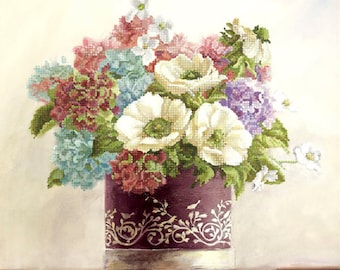 May include: A cross-stitch pattern featuring a bouquet of white anemones, blue and red hydrangeas, and small white flowers in a dark purple cylindrical vase with a white decorative scroll pattern. The Tela Artis logo is in the bottom right corner.