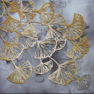 Könnte beinhalten: Nahaufnahme einer Perlen-Stickerei mit einer Gruppe von Ginkgoblättern in Gold- und Silbertönen. Die Blätter sind in einem kaskadierenden Muster angeordnet und bilden ein zartes und filigranes Design.