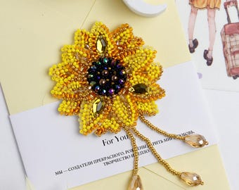 May include: A beaded sunflower brooch with a yellow and orange center and gold beads. The brooch has a long gold chain with three dangling crystal beads.