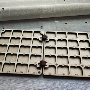K&ouml;nnte beinhalten: Ein h&ouml;lzerner Bastel-Organizer mit 40 nummerierten quadratischen F&auml;chern, die durch ein Scharnier verbunden sind. Der Organizer ist aus hellfarbigem Holz gefertigt und f&uuml;r kleine Gegenst&auml;nde konzipiert. Die Zahlen 1-40 sind in das Holz ge&auml;tzt.