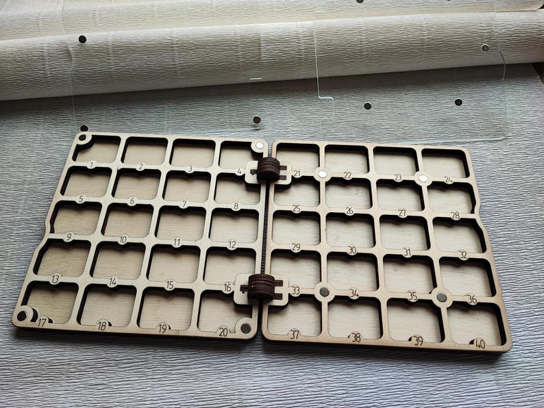 K&ouml;nnte beinhalten: Ein h&ouml;lzerner Bastel-Organizer mit 40 nummerierten quadratischen F&auml;chern, die durch ein Scharnier verbunden sind. Der Organizer ist aus hellfarbigem Holz gefertigt und f&uuml;r kleine Gegenst&auml;nde konzipiert. Die Zahlen 1-40 sind in das Holz ge&auml;tzt.