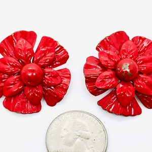 May include: A pair of red metal flower earrings. Each earring features a red flower with a raised center and petals that have a textured finish.