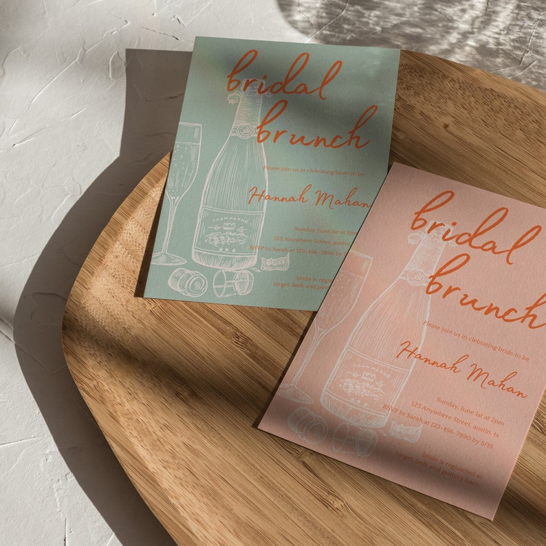 May include: Two peach and light blue bridal brunch invitations with a champagne bottle and glass illustration. The text on the invitations reads "bridal brunch" and "Hannah Mahan".