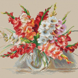 May include: A cross-stitch design of a floral arrangement in a clear glass vase. The bouquet features red, orange, white, and pink gladiolus flowers with green stems and leaves. The background is a neutral beige color.