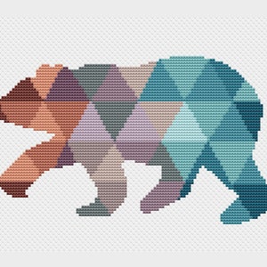 Puede incluir: Un diseño de punto de cruz de patrón geométrico de un oso en tonos marrones, morados, azul verdoso y grises.