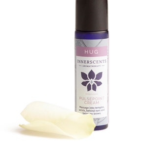 Puede incluir: Un frasco azul y blanco con rodillo, etiquetado como "HUG INNERSCENTS AROMATHERAPY PULSEPOINT CREAM" con instrucciones para masajear en las sienes, las muñecas, detrás de las orejas y entre las cejas.
