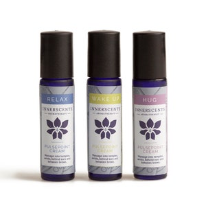Puede incluir: Tres frascos de vidrio azul con tapas negras. Cada frasco tiene una etiqueta de color diferente con las palabras "Relax", "Wake Up" y "Hug" en ellas. Las etiquetas también dicen "Innerscents Aromatherapy" y "Pulsepoint Cream".