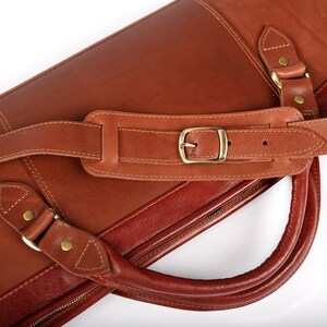 May include: A brown leather carrying case with a shoulder strap and a handle. The case has a zipper closure and a brass buckle.