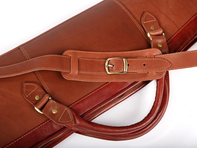 May include: A brown leather carrying case with a shoulder strap and a handle. The case has a zipper closure and a brass buckle.