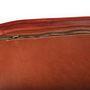 May include: Close-up of a brown leather bag with a zipper closure. The zipper has a brass pull with the word "UNIVERSAL" engraved on it.