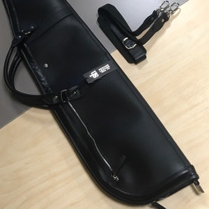 May include: Black leather gun case with a zipper and a shoulder strap. The case has a tag that says "Genuine Leather".