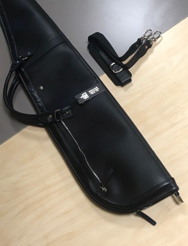 May include: Black leather gun case with a zipper and a shoulder strap. The case has a tag that says "Genuine Leather".